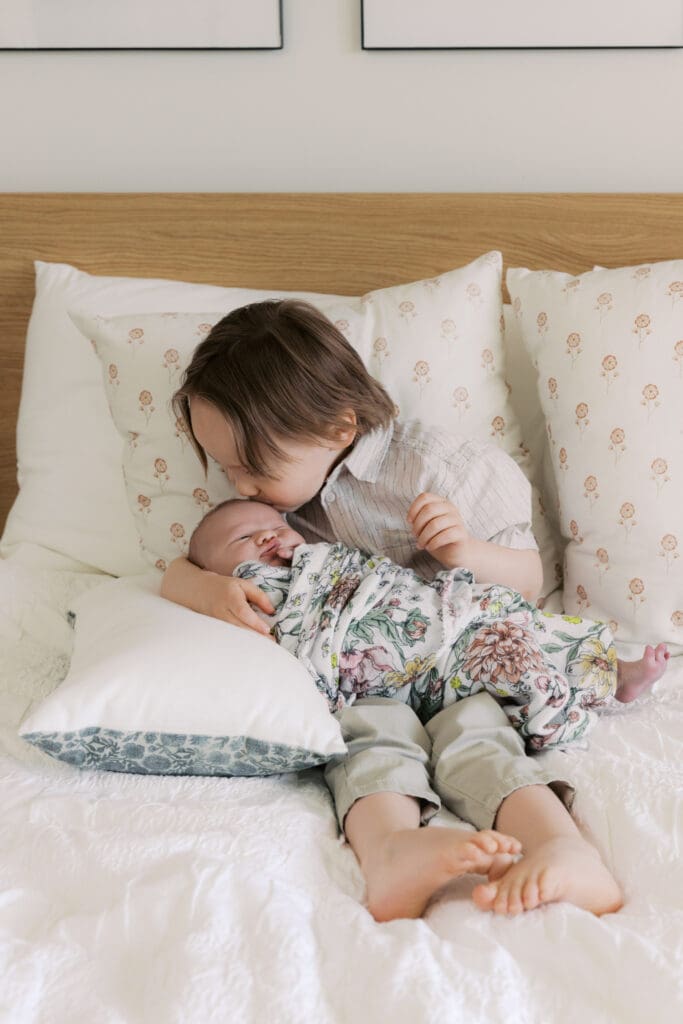 brother on bed holding new born baby sister