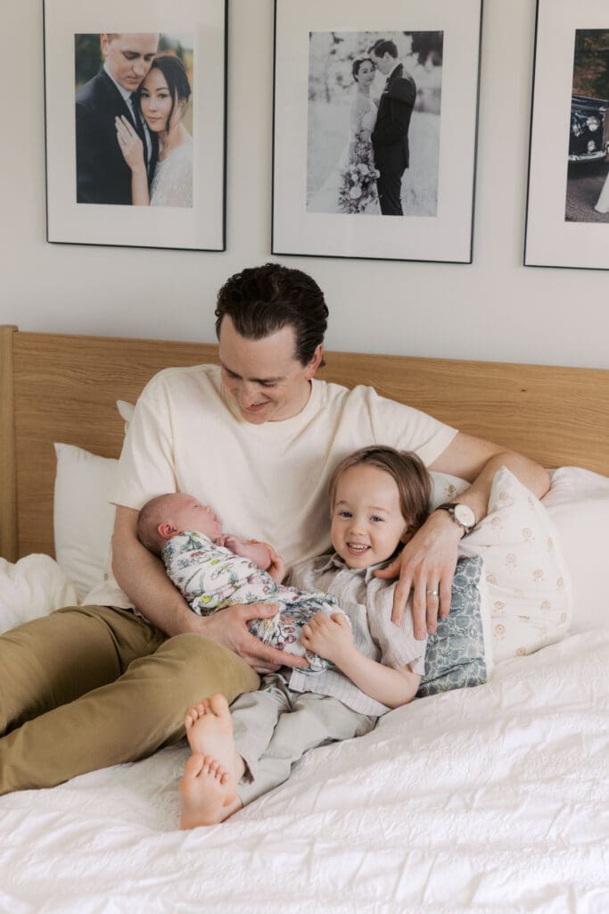 brother and dad smiling with new born baby sister